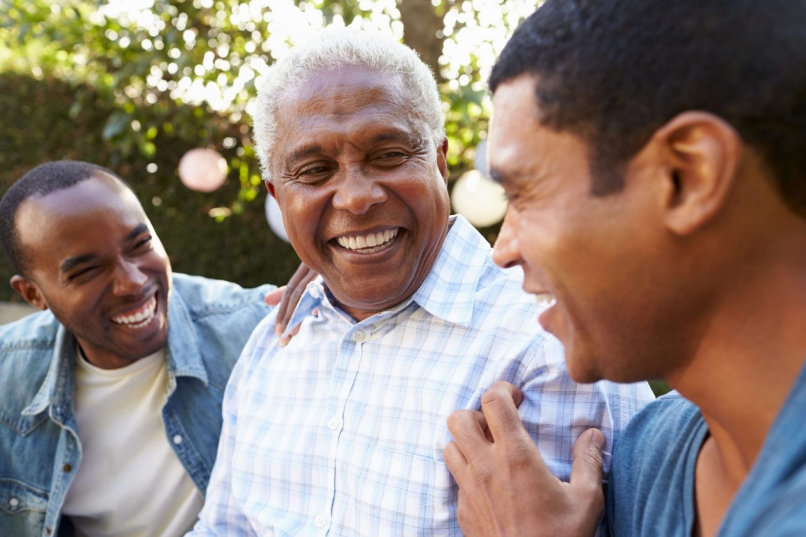 Three men from different generations smiling and laughing together outdoors.