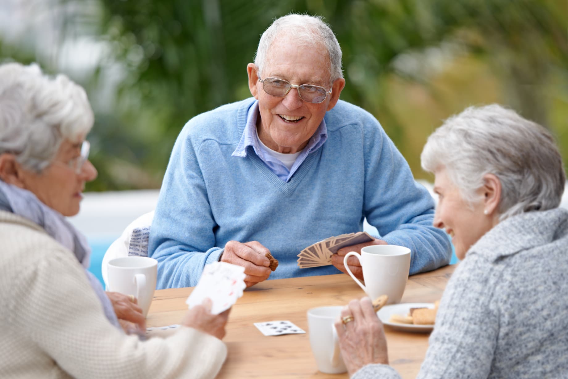 Two older adult women and a senior man smile while playing cards together